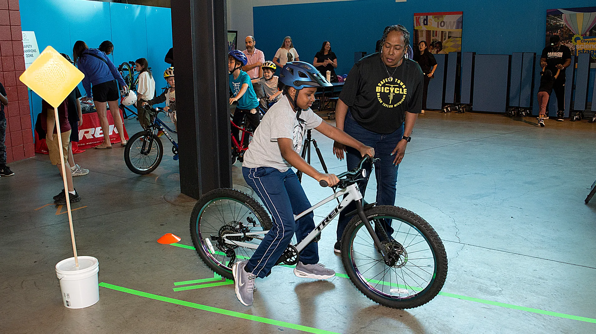 An instructor guiding a young rider through a marked course at a Bicycle Safety Town session